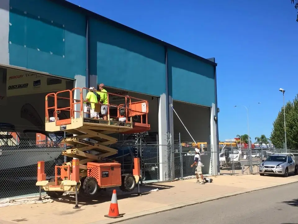 Scissor lift beside a teal warehouse wall being coated